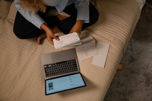a girl is checking the cheque with laptop while sitting in the bed
